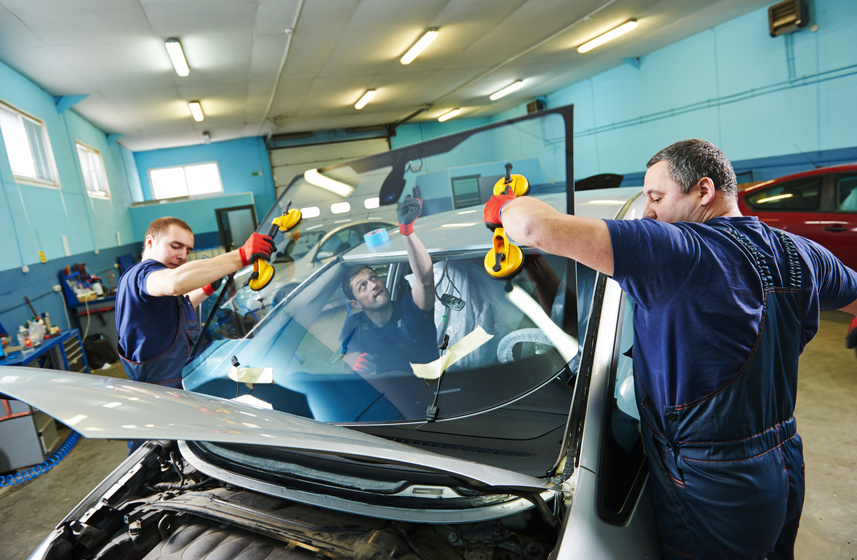 Automobile glaziers workers replacing windscreen or windshield of a car in auto service station garage